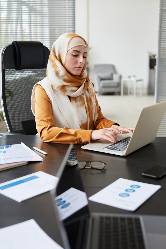 Professional Muslim businesswoman working on a laptop in a modern office setting. Ideal for business and diversity themes.