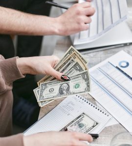 Two individuals counting dollar bills and reviewing financial documents indoors.